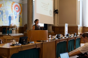 A speaker at the lectern below the chamber's mural
