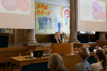A speaker at the lectern with figures on the screens