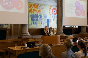 A speaker at the lectern with figures on the screens