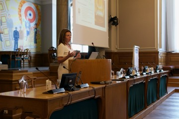 A speaker at the lectern below the chamber's mural